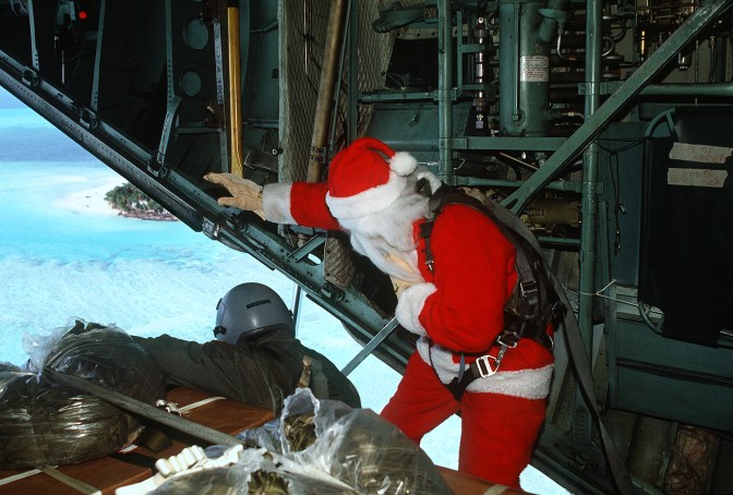 Dec. 14, 1990. Santa Claus (Capt. Mike d'Albertis, 605th Military Airlift Support Squadron) and Staff Sgt. Tony Thompson, loadmaster with the 21st Tactical Airlift Squadron, watch as a Christmas Drop container is parachuted toward its destination. The annual airdrop is a humanitarian effort providing aid to needy islanders throughout Micronesia during the Christmas season. (U.S Air Force Photograph by Tech. Sgt. James Ferguson/Released)